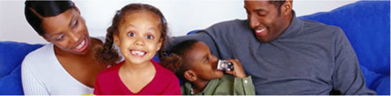 picture of family, a mother, father, and their two children. The daughter is grinning and looking forward, with the mother smiling and looking at her, while the father and son are playful and looking at each other.